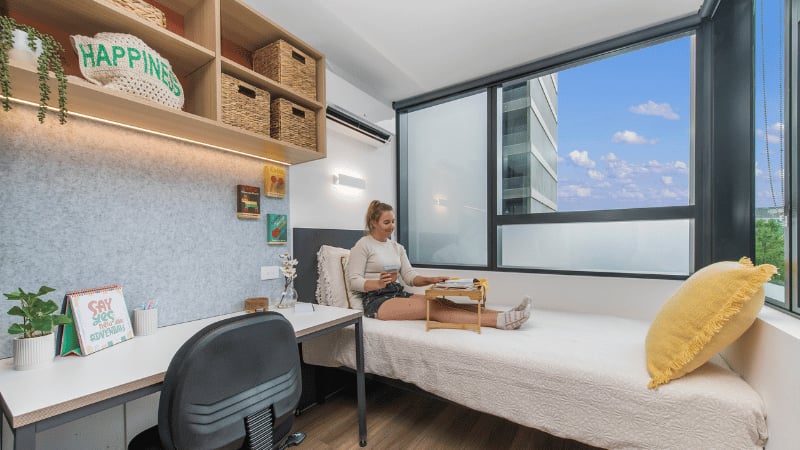 Desk bed shelves woman holding tray bedroom at UniLodge Melbourne Flagstaff in Melbourne Student Accommodation