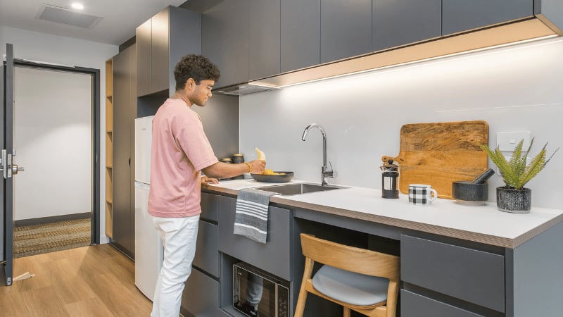 Young man cooking at modern kitchen counter with sink Kitchen at UniLodge Melbourne Flagstaff in Melbourne Student Accommodation