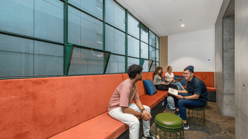 Students on orange bench with laptops communal area at UniLodge Melbourne Flagstaff in Melbourne Student Accommodation