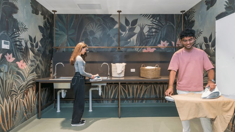 Students ironing and washing with tropical mural Laundry room at UniLodge Melbourne Flagstaff in Melbourne Student Accommodation