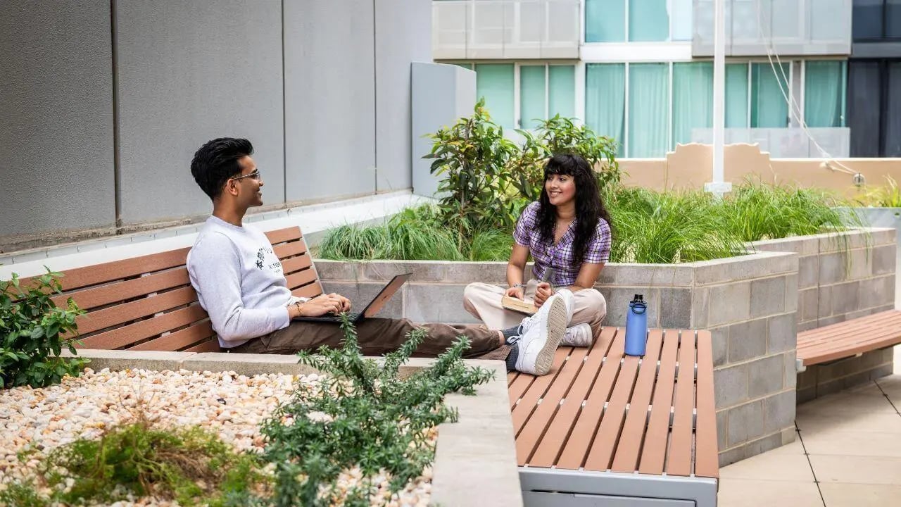 Students on benches with laptop and book outdoor area at UniLodge Melbourne Flagstaff in Melbourne Student Accommodation