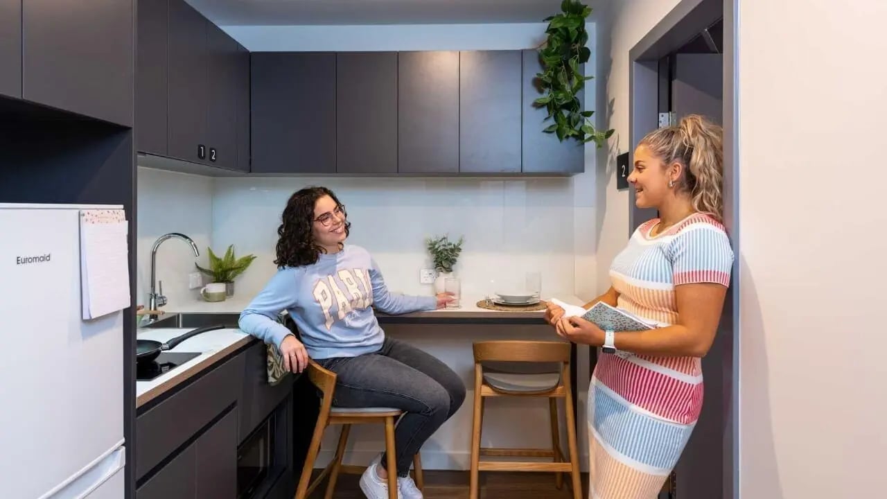 Two women kitchen counter and chairs kitchen at UniLodge Melbourne Central in Melbourne Student Accommodation