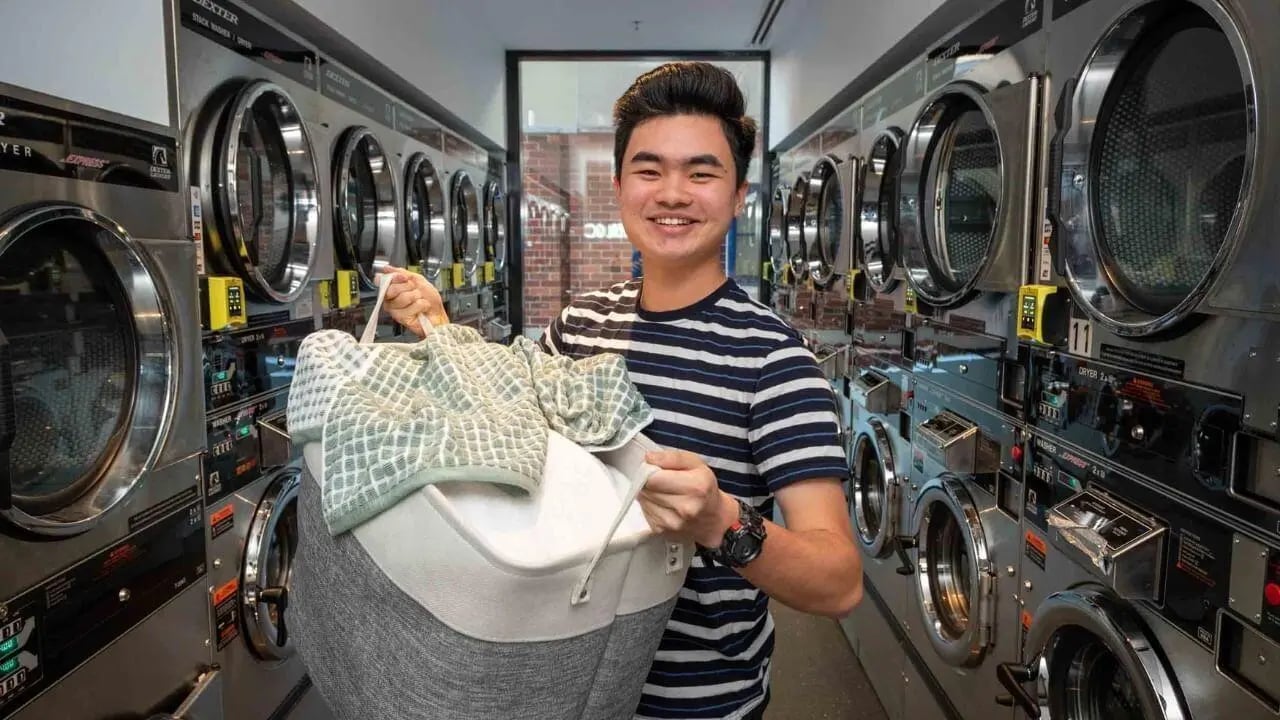 Man with laundry basket among washers and dryers laundry area at UniLodge Melbourne Central in Melbourne Student Accommodation