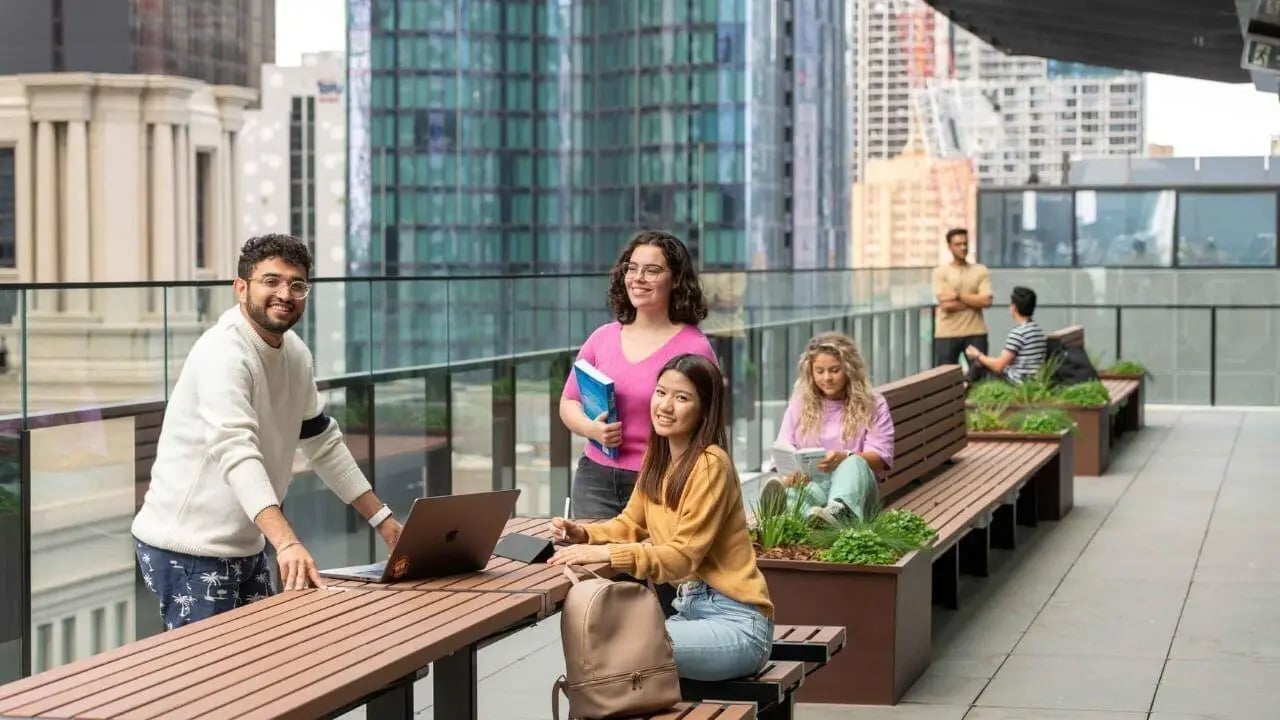 Students studying on wooden benches with laptop exterior at UniLodge Melbourne Central in Melbourne Student Accommodation