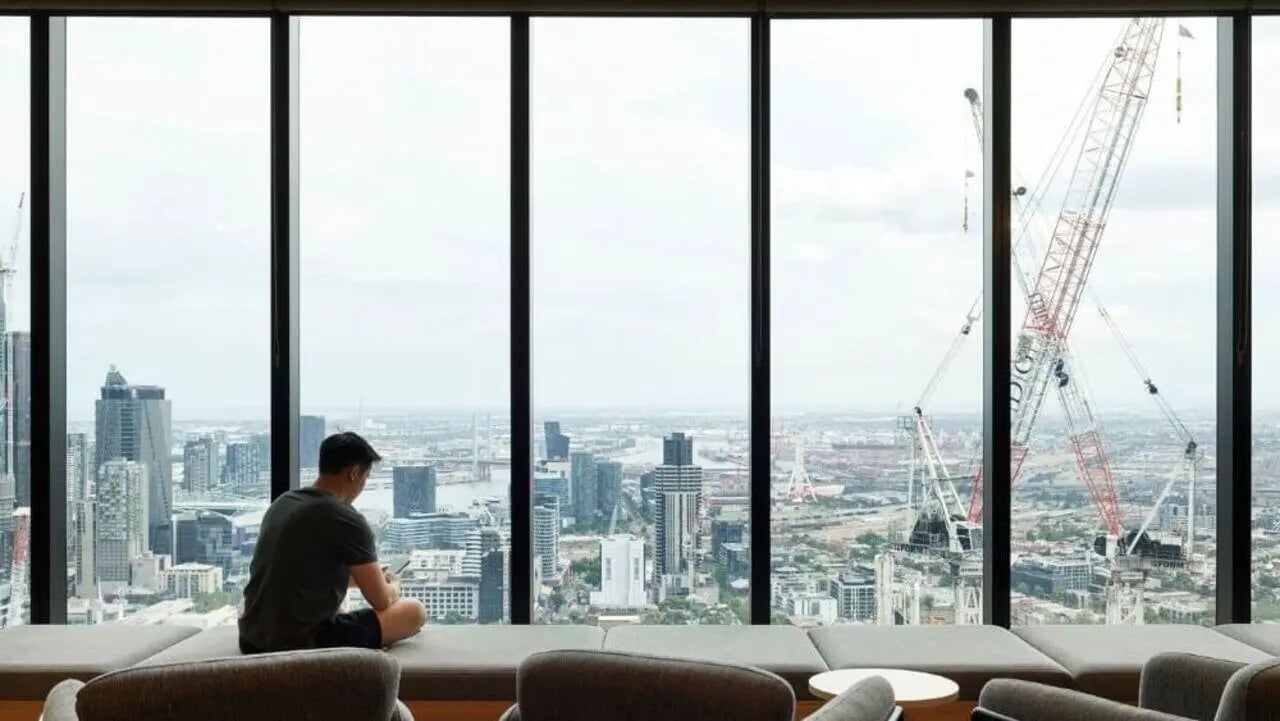 Man sitting on sofa enjoying city view living room at Unilodge Melbourne City in Melbourne Student Accommodation