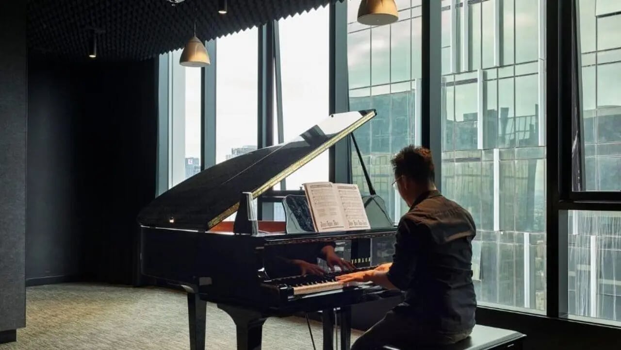 Man playing grand piano near large windows common room at Unilodge Melbourne City in Melbourne Student Accommodation