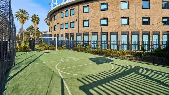 Small soccer court with building and palm trees exterior at UniLodge Park Avenue in Melbourne Student Accommodation
