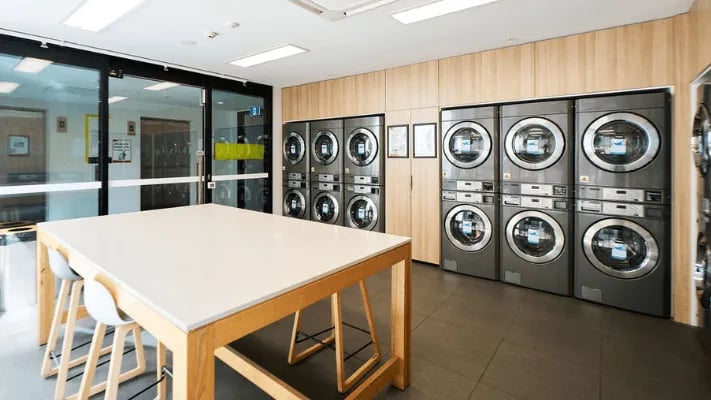 Laundry machines and table with chairs laundry room at UniLodge Park Avenue in Melbourne Student Accommodation