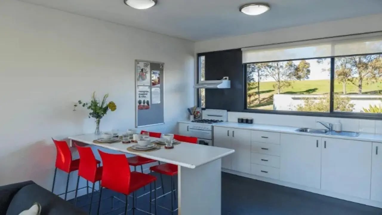 Dining table red chairs kitchen counter stove window kitchen at Western Sydney University Campbelltown Village in Sydney Student Accommodation