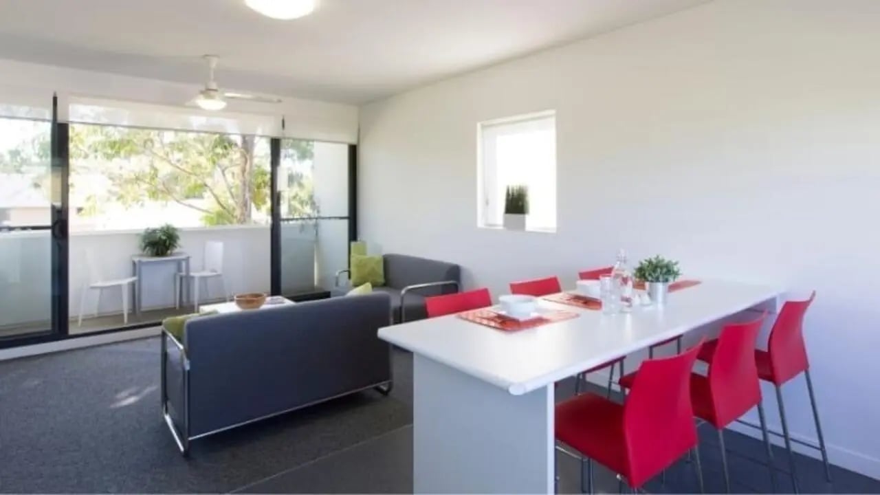 Dining table with red chairs lounge area living room at Western Sydney University Campbelltown Village in Sydney Student Accommodation