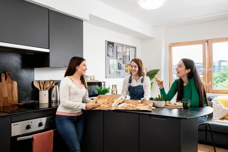 Three friends eating pizza in modern kitchen at Piccadilly Court in London Student Accommodation