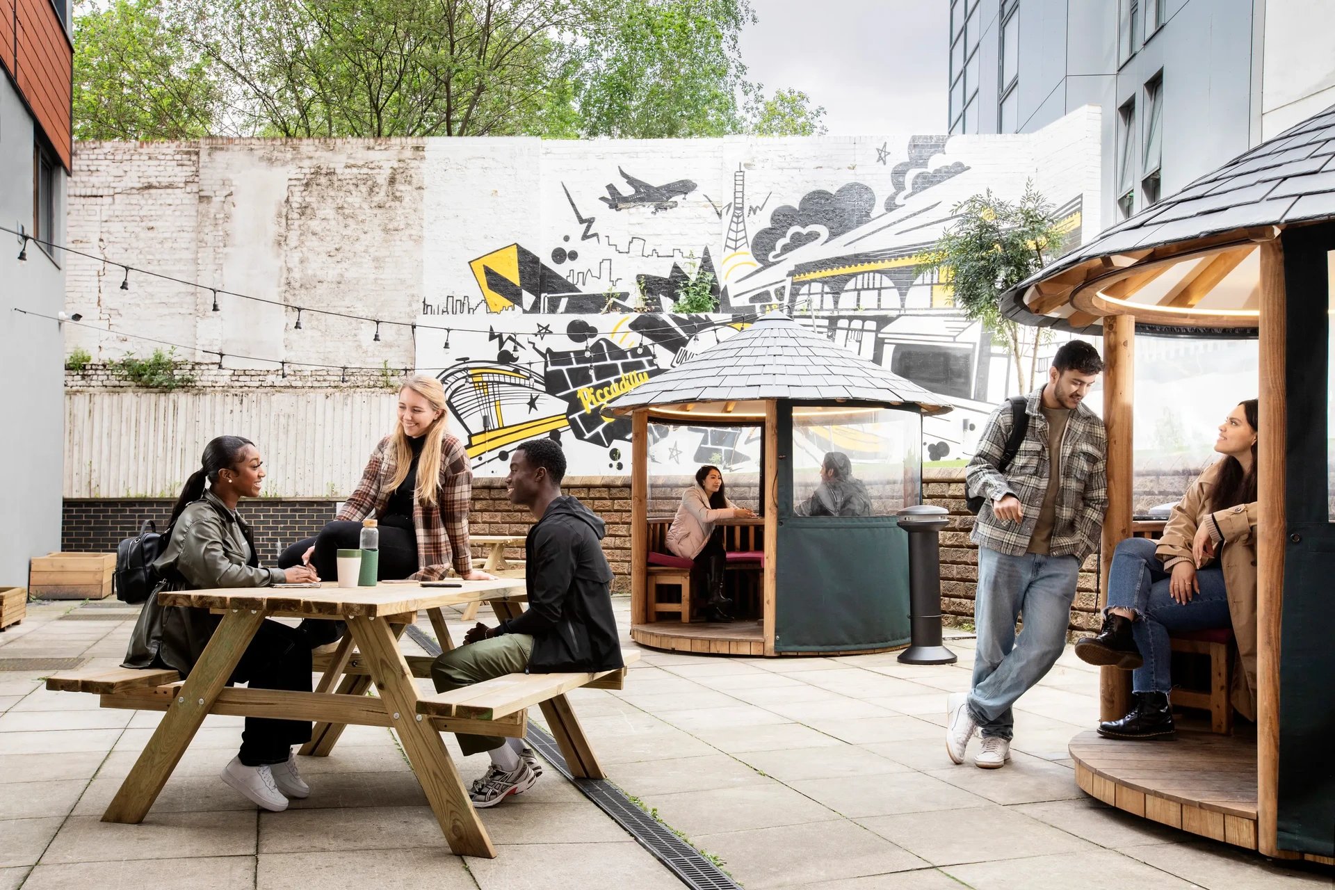 Students on picnic tables and pods exterior at Piccadilly Court in London Student Accommodation