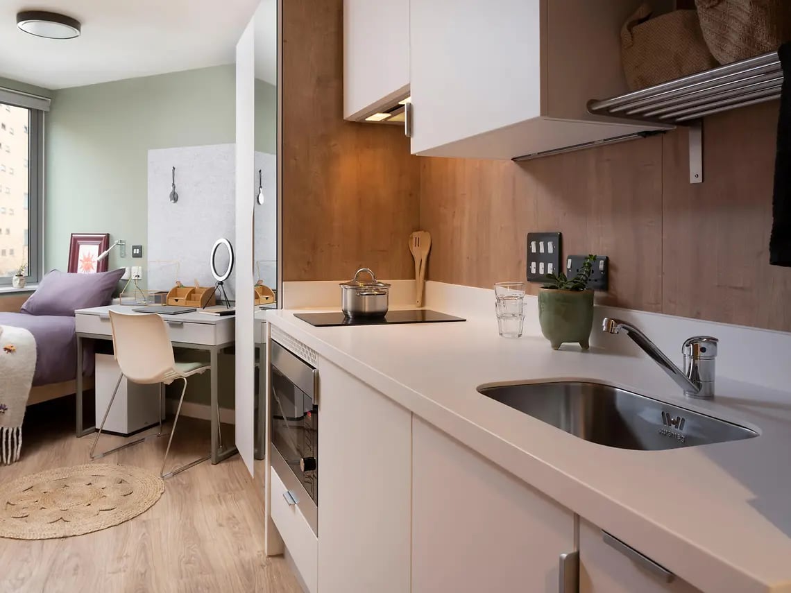 Bed desk chair and kitchen area living room at The Curve in London Student Accommodation