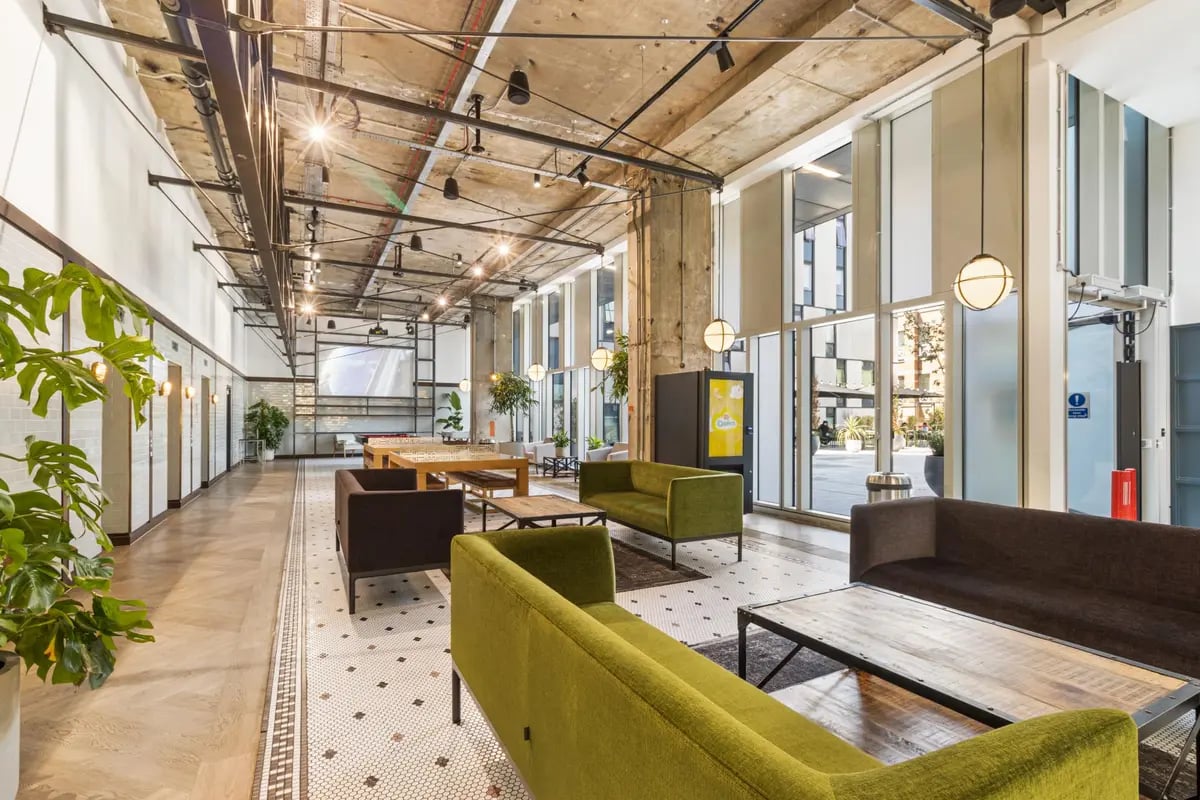 Green couches and wooden tables in common area at Chapter Kings Cross in London Student Accommodation