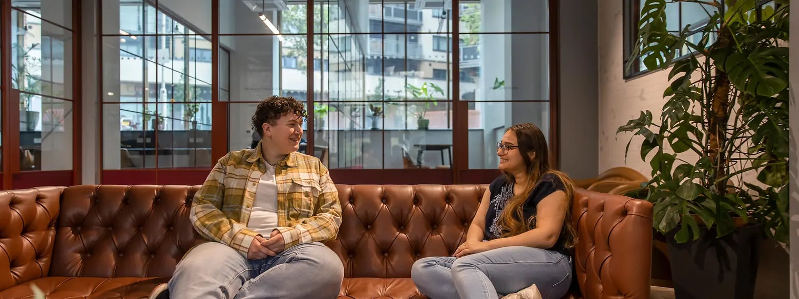 Two students relax on a brown leather sofa living room at The Valentine London in London Student Accommodation