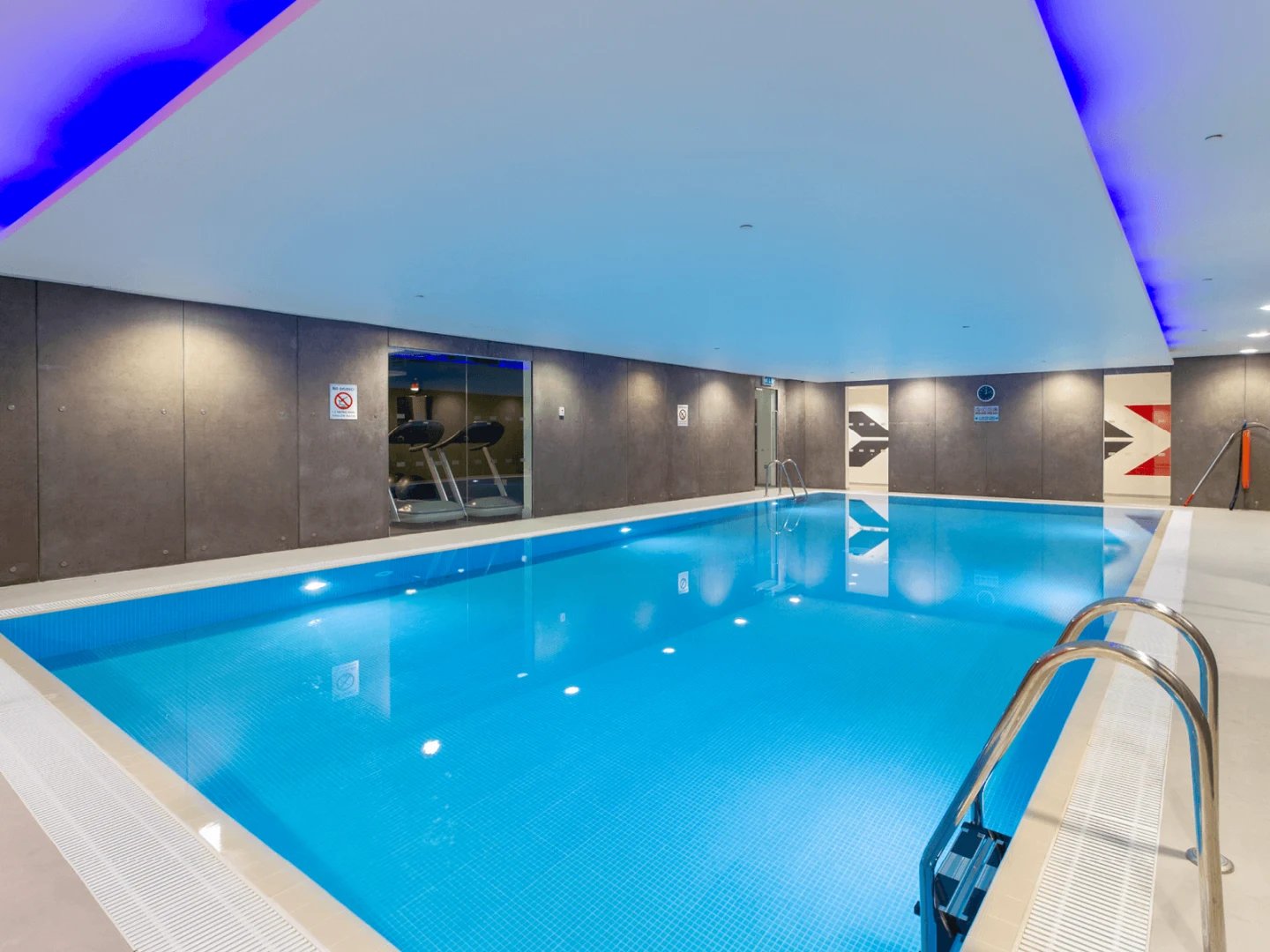 Indoor swimming pool with treadmills visible through window playing area at Spring Mews in London Student Accommodation