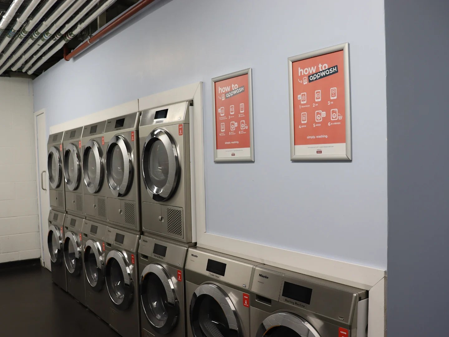 Stacked washing machines with instructional posters laundry room at Spring Mews in London Student Accommodation