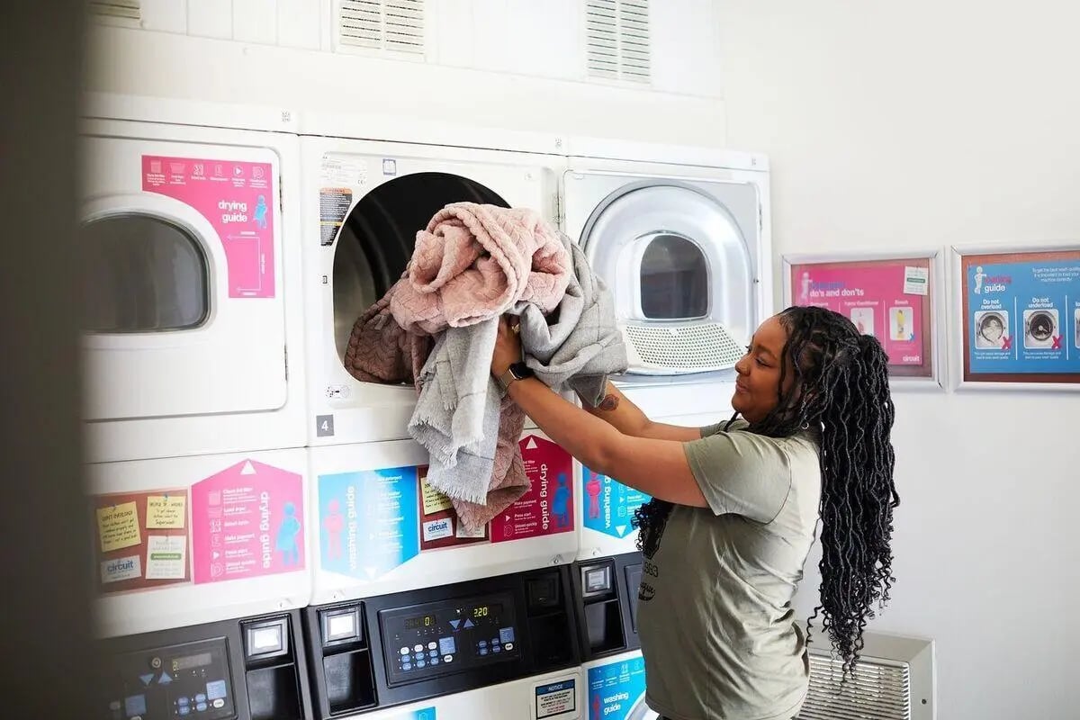 Woman folding laundry into dryer laundry room at Collegiate Dashwood Studios in London Student Accommodation