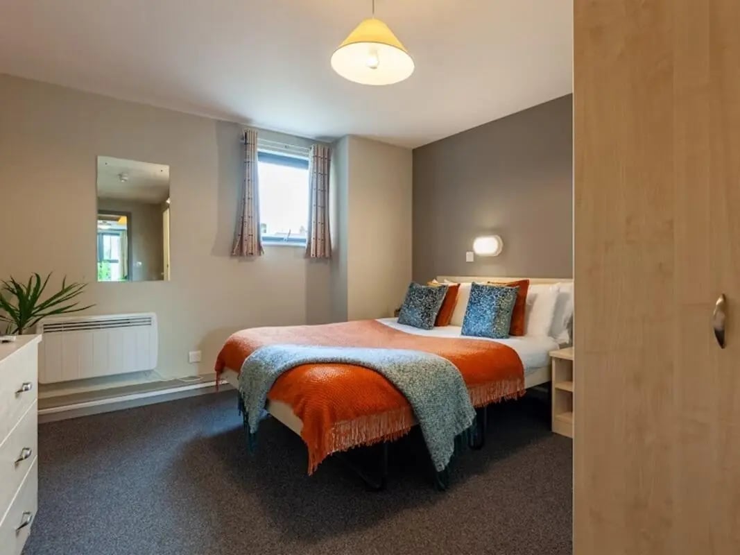 Bed with orange throw pillows dresser mirror bedroom at Crown House - Reading in Reading Student Accommodation