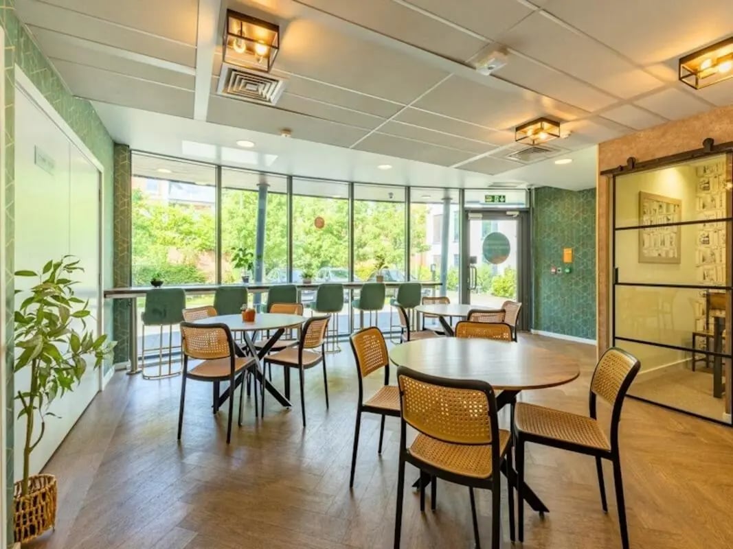 Round tables cane chairs plants large windows communal area at Kendrick Hall in Reading Student Accommodation