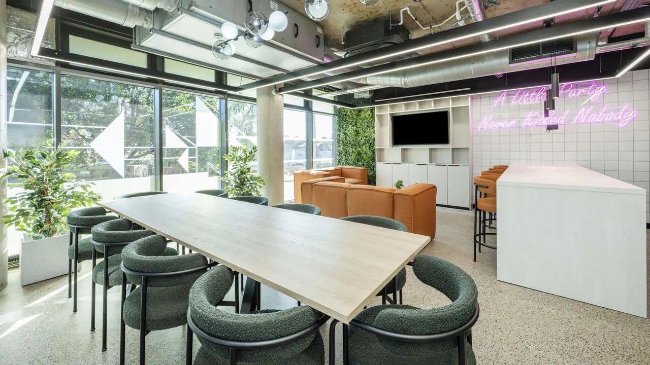 Long table green chairs orange sofa neon sign communal area at The Printworks in Exeter Student Accommodation