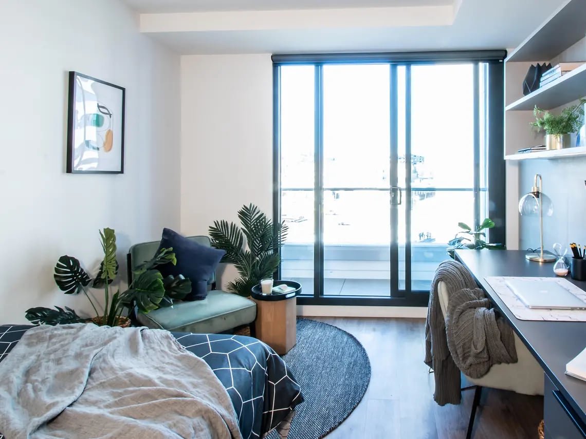Bed plants chair desk with laptop Bedroom at Yugo University Square Melbourne in Melbourne Student Accommodation