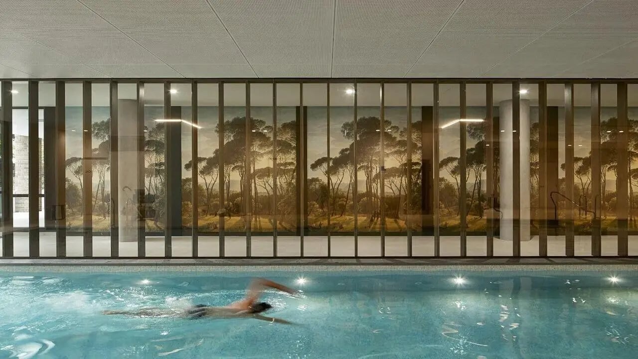 Person swimming in pool against scenic mural interior at Realm Caulfield in Melbourne Student Accommodation