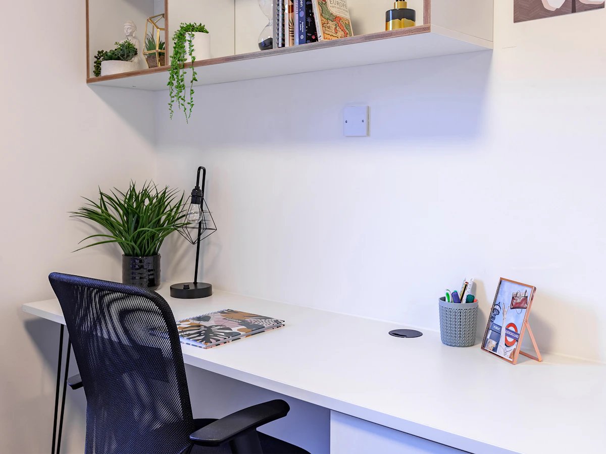 Desk plant lamp notebook pens photo study area at Fulham Palace Studios in London Student Accommodation