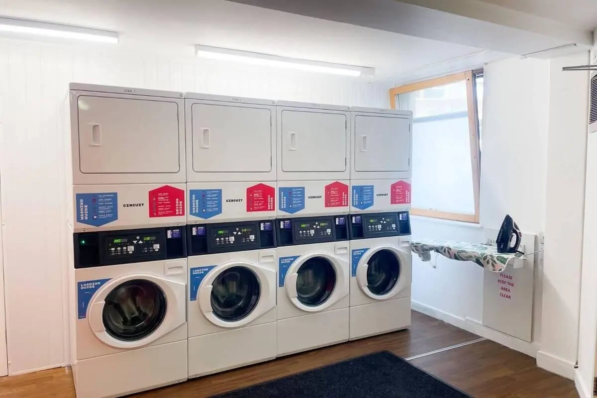 Stack of washing machines dryers ironing board laundry area at Don Gratton House in London Student Accommodation