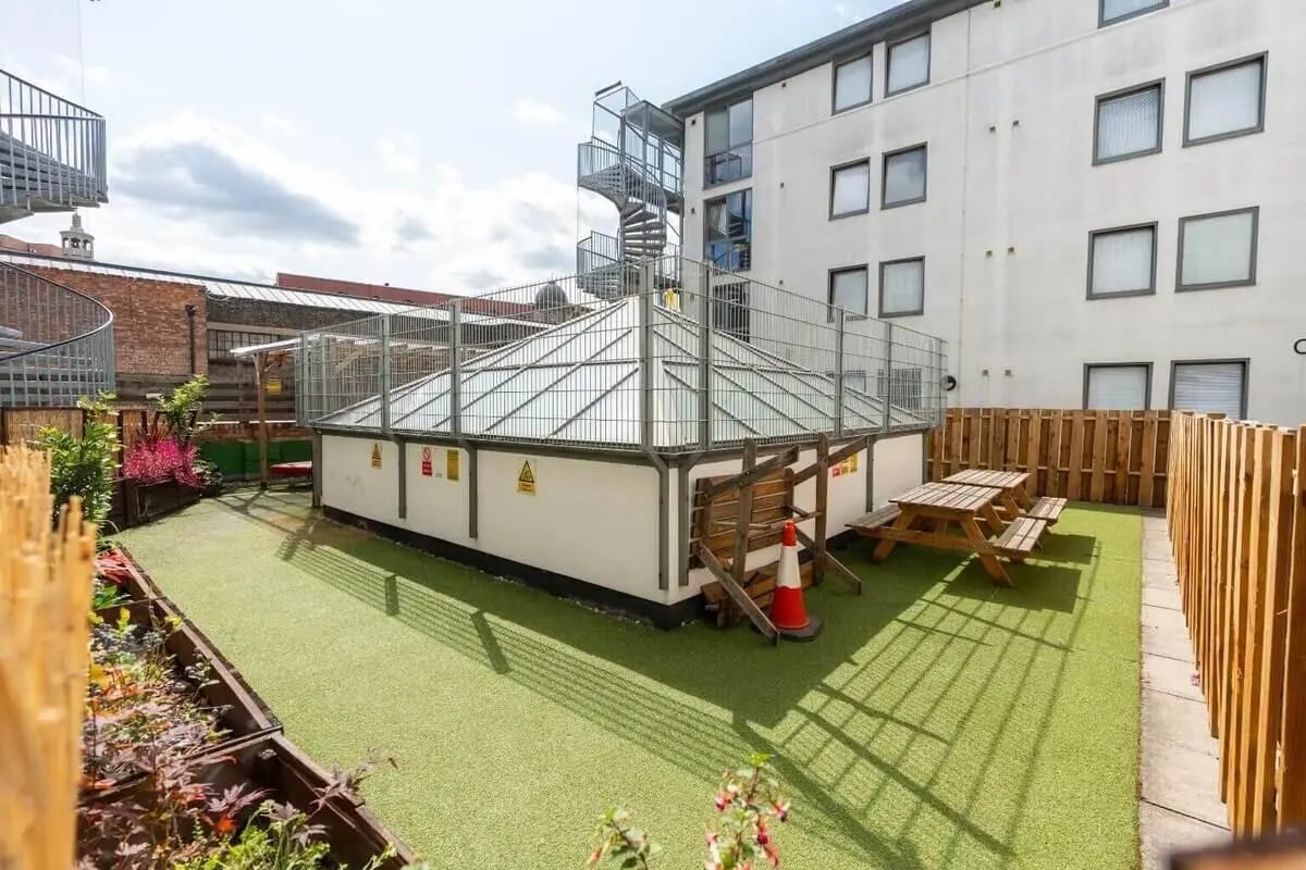 Picnic tables and planters on artificial turf exterior at Don Gratton House in London Student Accommodation