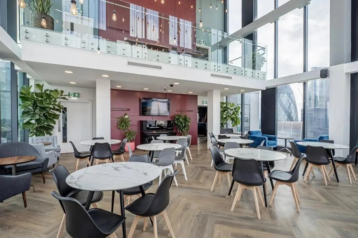 Tables chairs plants piano TV playing area at Chapter Spitalfields in London Student Accommodation