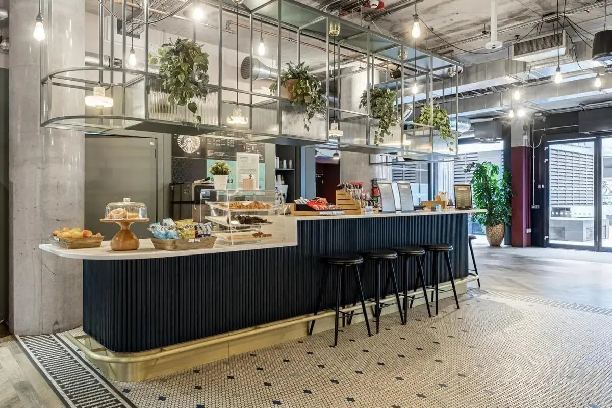 Bar with stools plants and food kitchen at Chapter Spitalfields in London Student Accommodation