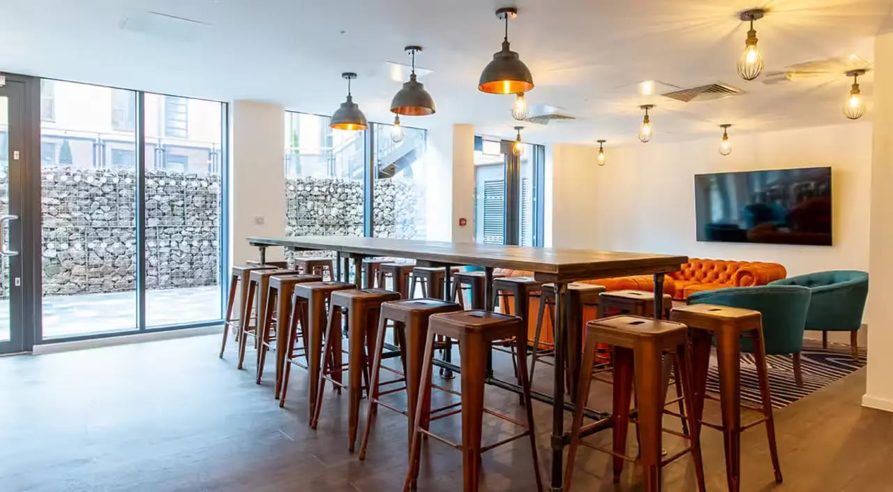 Long table stools orange sofa teal chairs living room at Dean Street Works in Bristol Student Accommodation