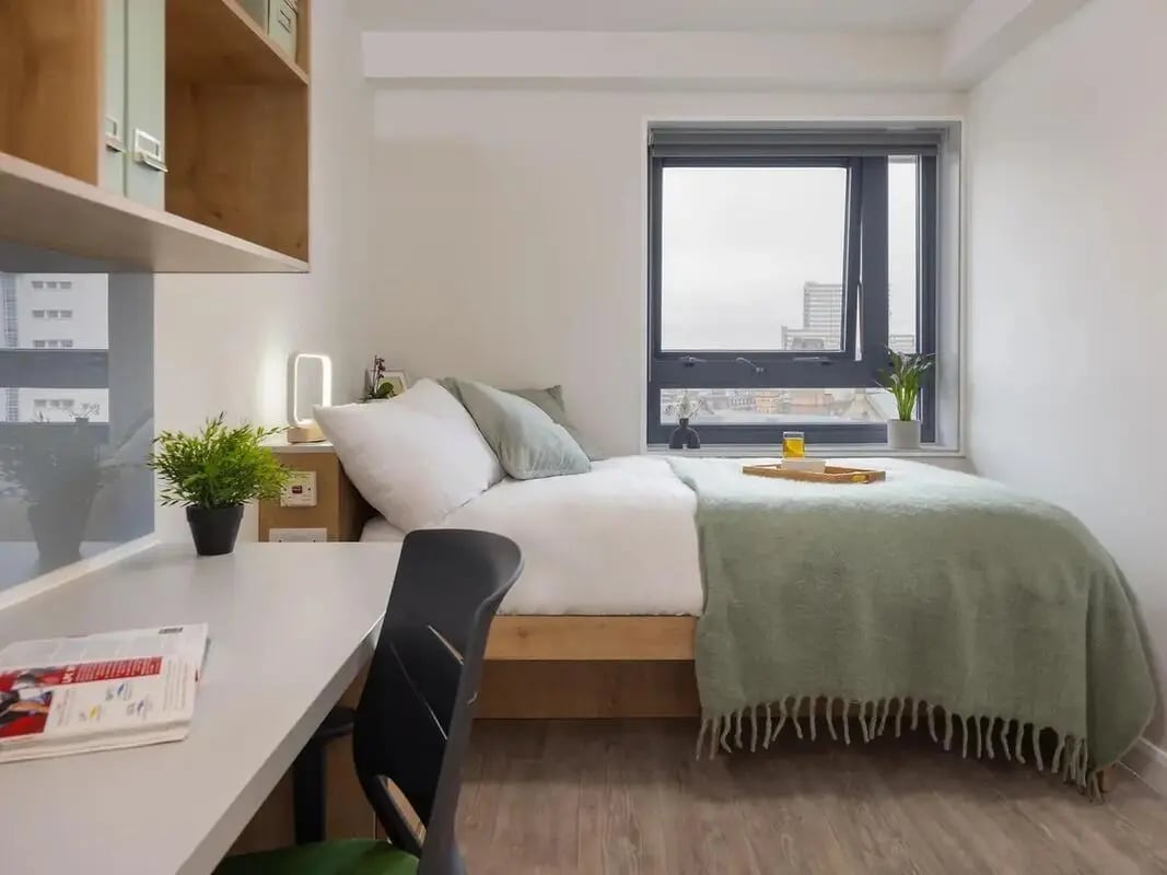 Bed with green blanket desk lamp and plant Bedroom at Yugo Goldsmith Court in Nottingham Student Accommodation