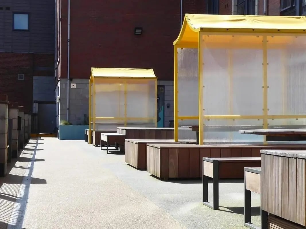 Wooden benches under yellow shelters outdoor area at Yugo Goldsmith Court in Nottingham Student Accommodation