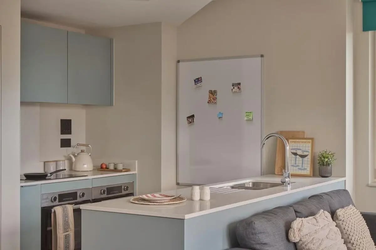 Kitchenette with stove kettle whiteboard and sofa living area at Ark Canning Town in London Student Accommodation