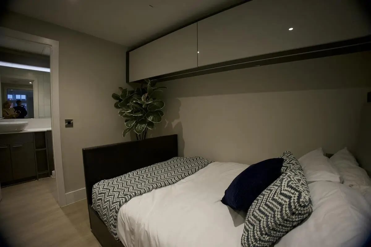 Bed with pillows throws storage cabinet plant bedroom at dwell 121 Princess Street in Manchester Student Accommodation
