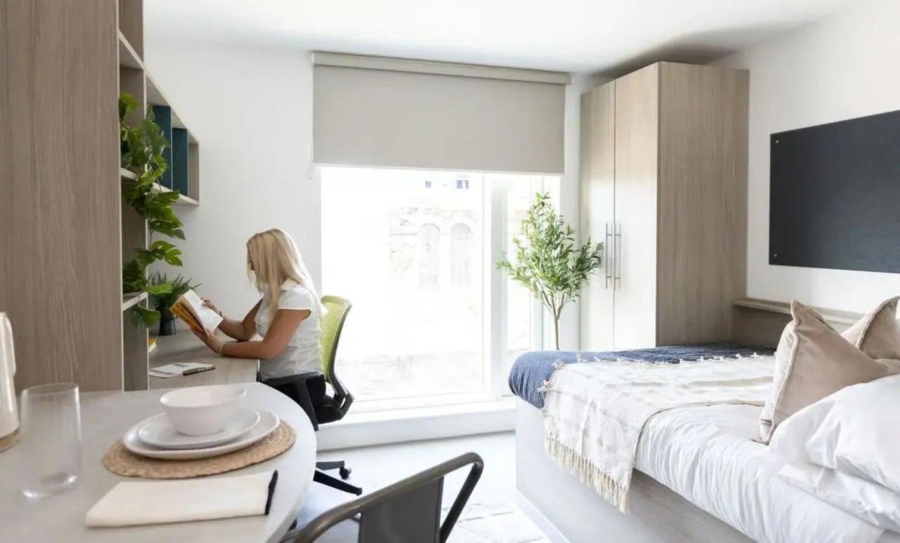 Woman reading at desk bed wardrobe study area bedroom at Timber Yard in Bristol Student Accommodation