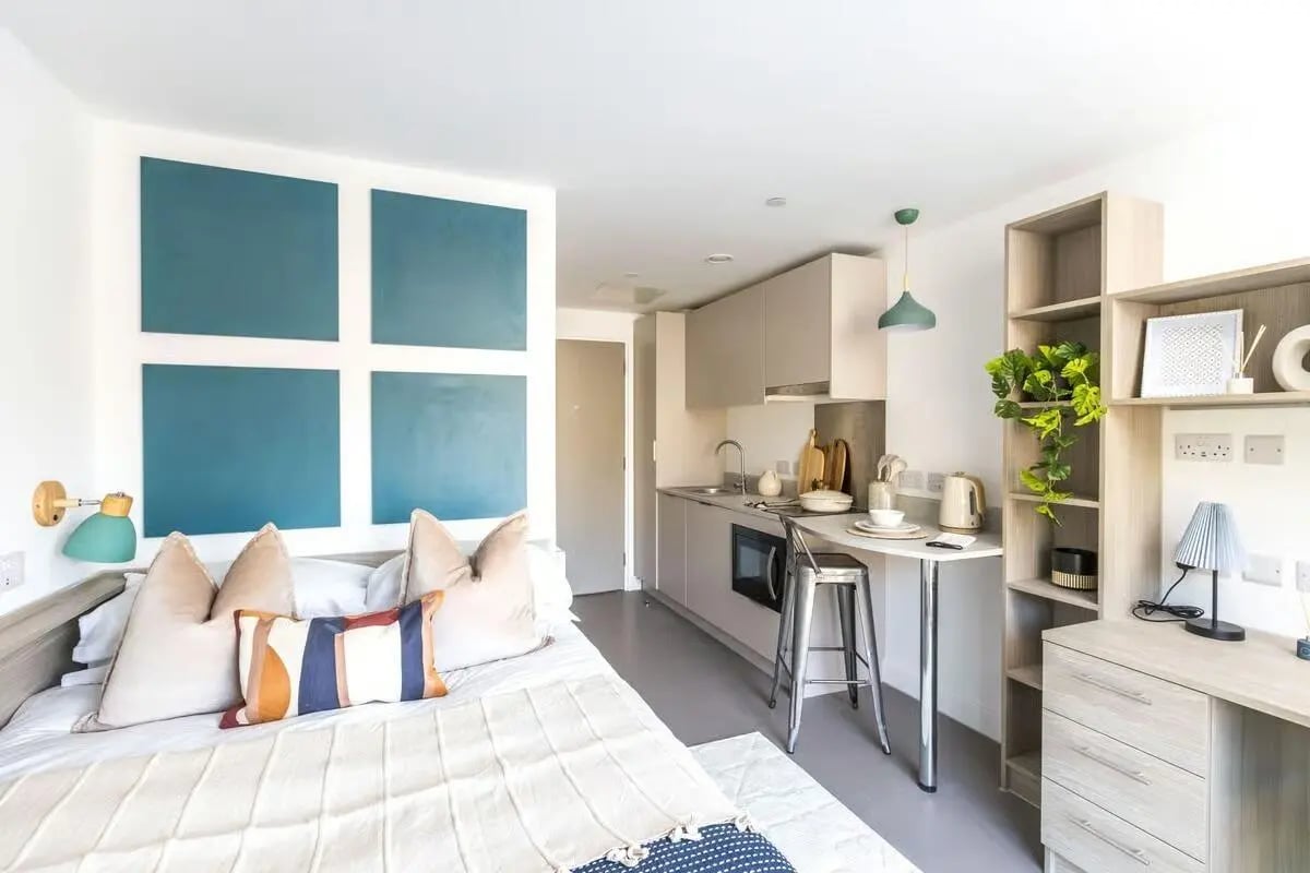 Bed with pillows kitchen counter and shelves studio apartment at Timber Yard in Bristol Student Accommodation