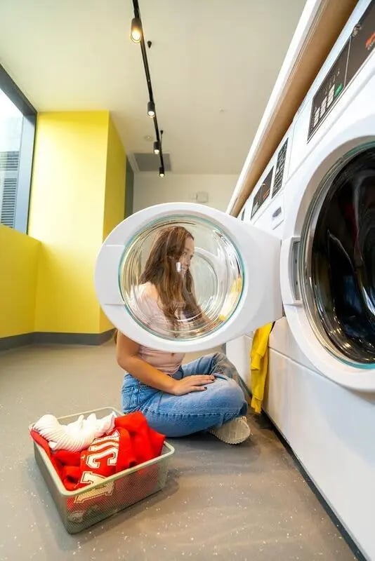 Woman loading laundry basket into dryer laundry room at Scape Kensington in Sydney Student Accommodation