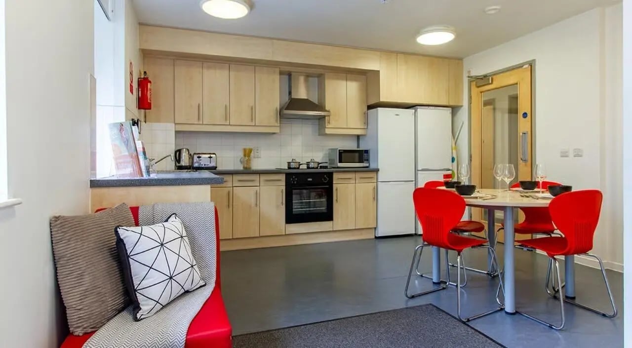 Red chairs round table kitchen cabinets and fridge kitchen at The Green in Bradford Student Accommodation