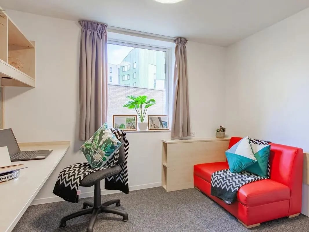 Desk chair red sofa window plants living room at The Green in Bradford Student Accommodation