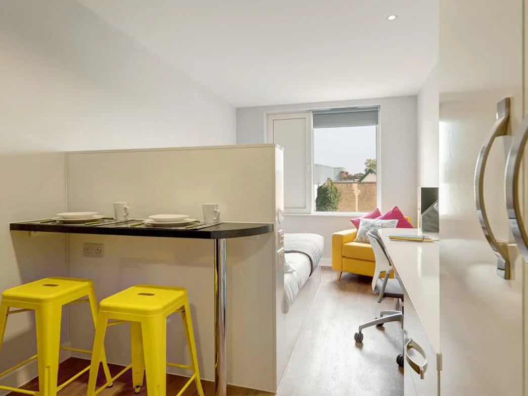 Table with yellow stools study desk yellow sofa bedroom living room study area at Glassyard Building in London Student Accommodation