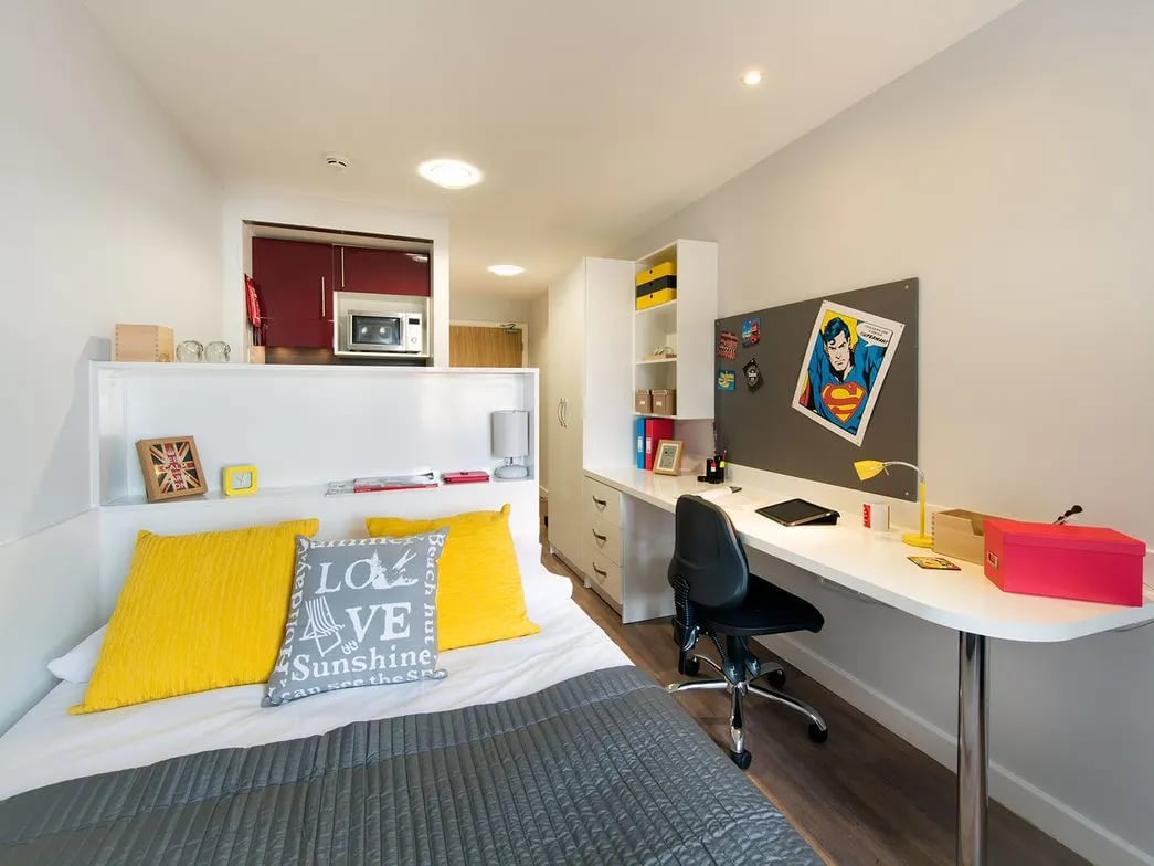 Bed study desk kitchen microwave and Superman poster studio apartment at Glassyard Building in London Student Accommodation