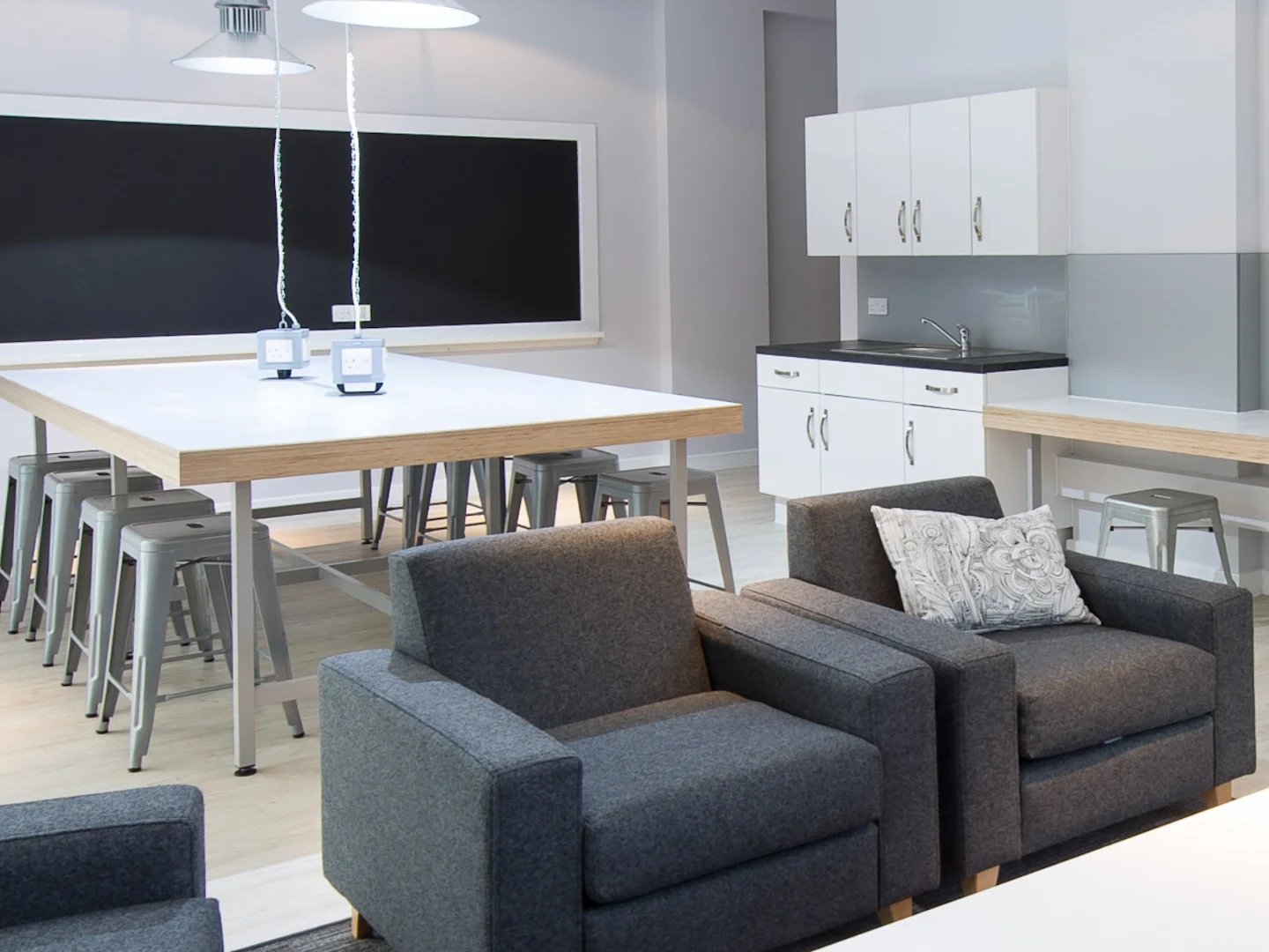 Dark grey armchairs table with stools kitchen area living room at Glassyard Building in London Student Accommodation