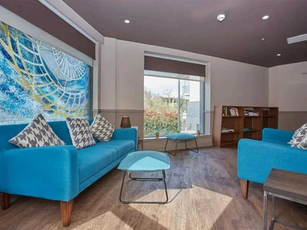 Blue sofas pillows stools bookshelf living room at Woodside House in Glasgow Student Accommodation