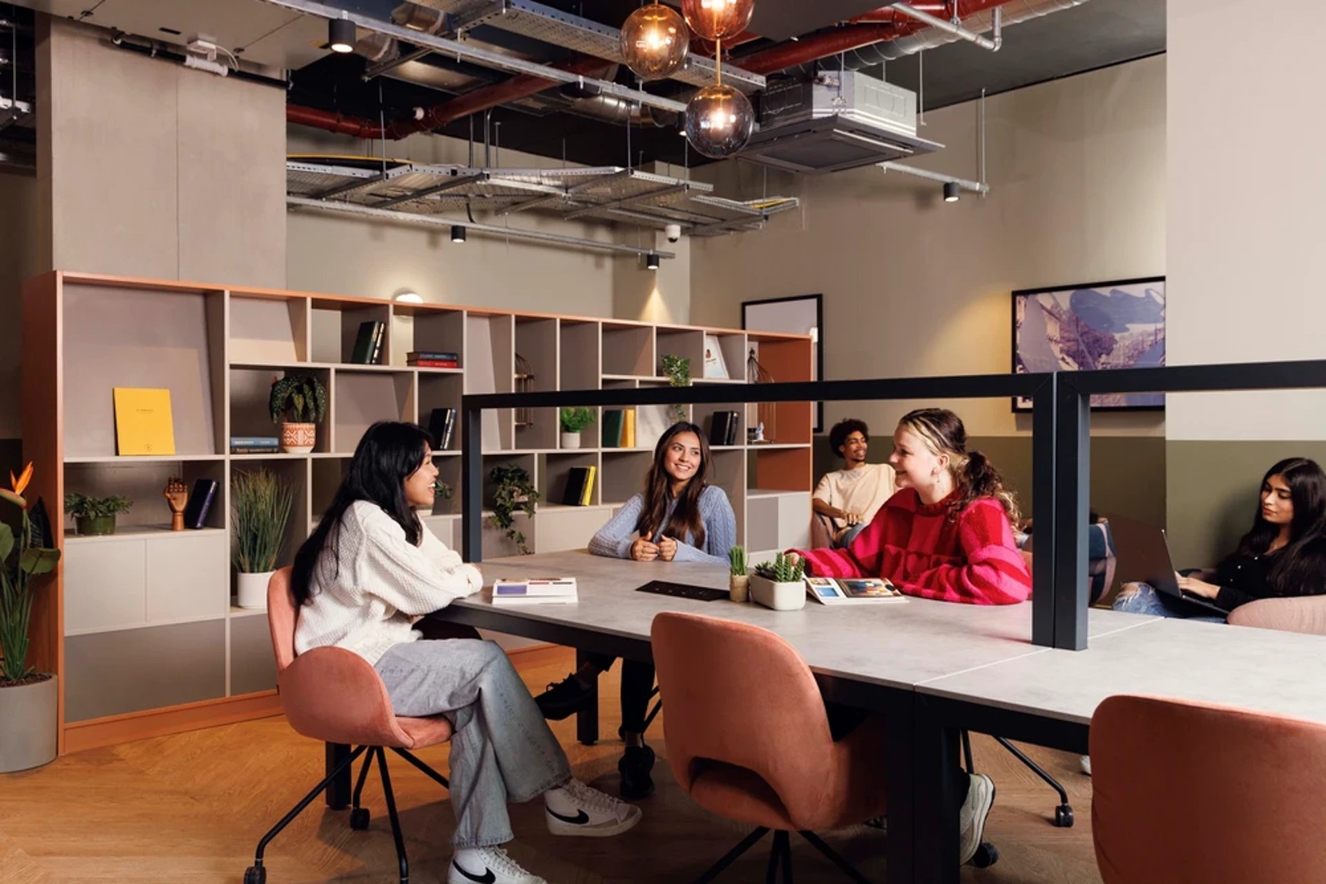 Students at large table near bookshelves communal area at Hayloft Point in London Student Accommodation