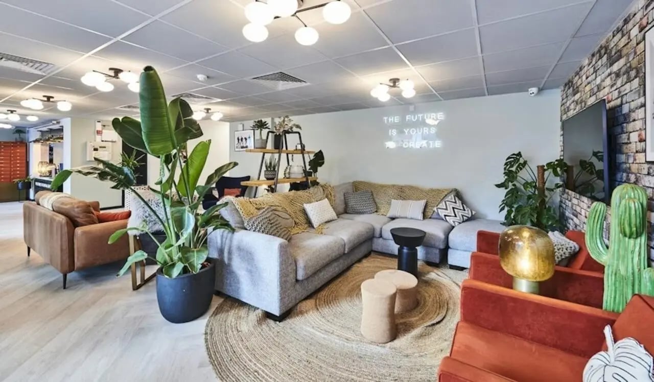 Modern lounge with sofas plants and neon sign living room at Capital Gate in Liverpool Student Accommodation