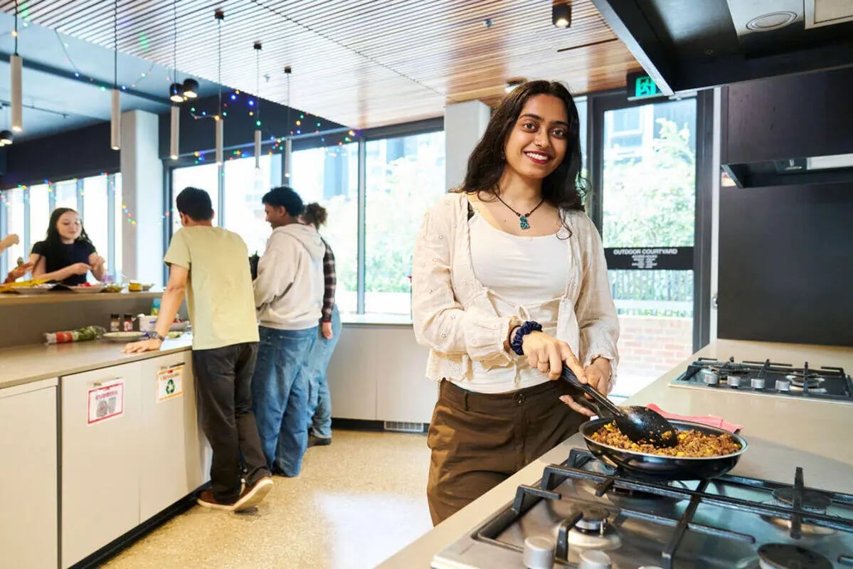 Young woman cooking in communal kitchen with students Kitchen at UniLodge Royal Melbourne in Melbourne Student Accommodation
