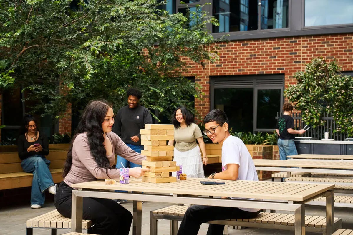 Students playing giant Jenga at outdoor tables playing area at UniLodge Royal Melbourne in Melbourne Student Accommodation